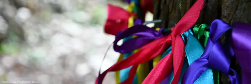 Lots of colourful fabric ribbons in bows tied to a fence.