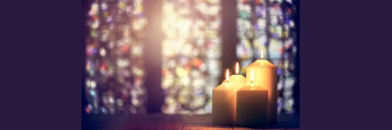 Four lit candles with stained glass window in the background.