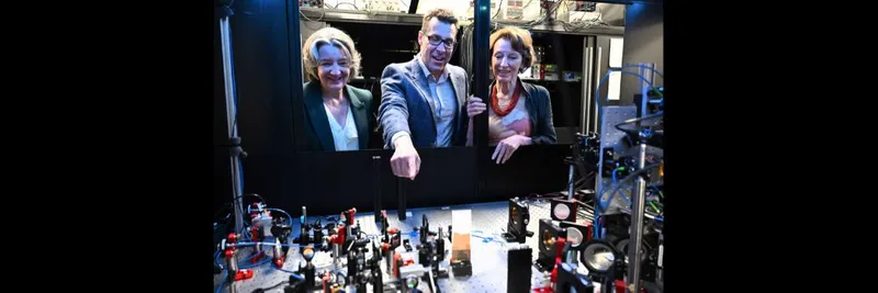 A man pointing to some scientific equipment, as he speaks with two women