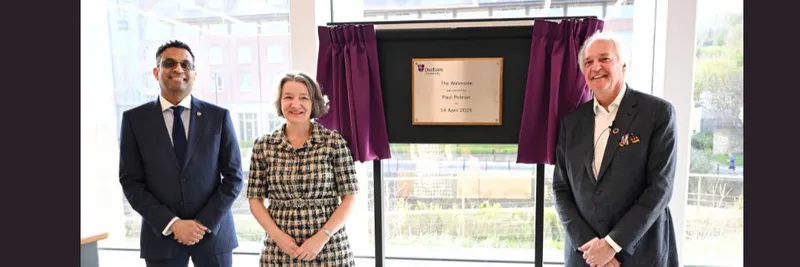 Three people standing in front of a plaque, revealed by a pulled curtain