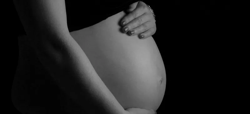 Black and white image showing a pregnant abdomen cradled with a pair of hands