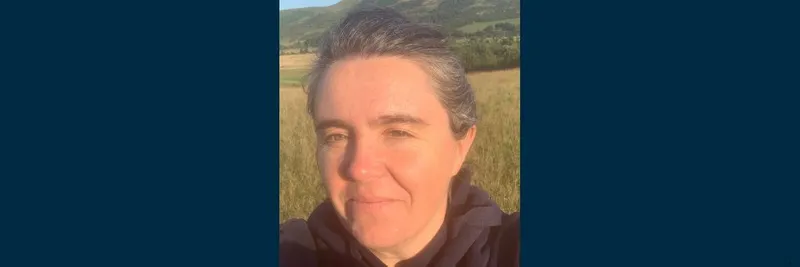 A head and shoulders close up photograph of Professor Sarah Semple. Sarah is smiling at the camera while standing in a field surrounded by countryside.