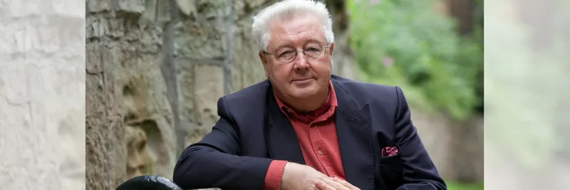 Douglas Davies sitting outside wearing a nave blazer and red shirt