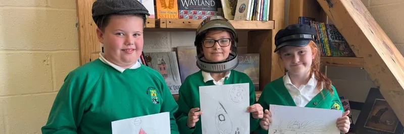 Three young people smile at the camera holding drawings they have made of rocket ships
