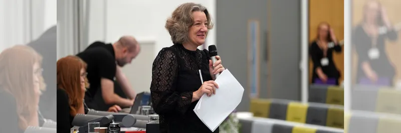 Vice-Chancellor Professor Karen O'Brien holding a microphone and smiling, wearing a black dress