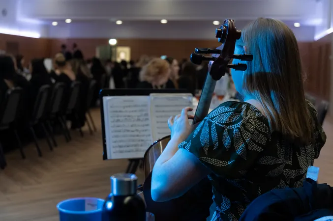 A musician plays the cello at a formal dinner event, with sheet music on a stand in front of her. Seated guests fill long tables in the softly lit room, creating an elegant and atmospheric setting at John Snow College.