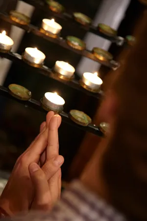 Closed hands with votive candles (prayer candles) behind