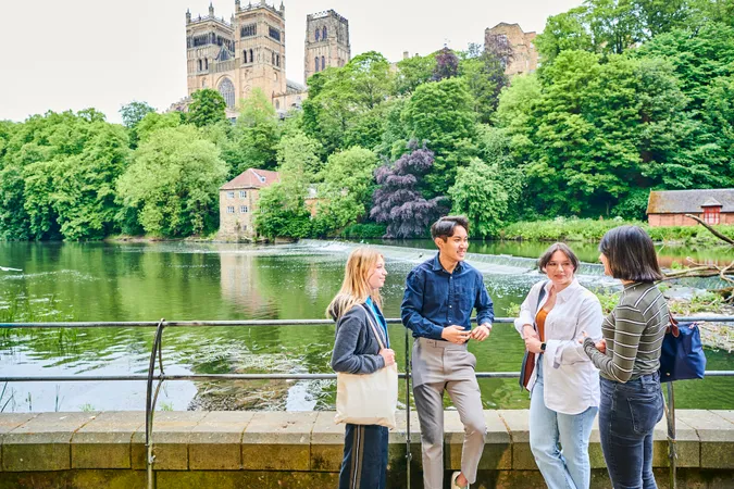 A group of students by a river in front of Durham Cathedral