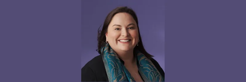 Woman with dark mid length hair wearing a jacket and scarf smiling