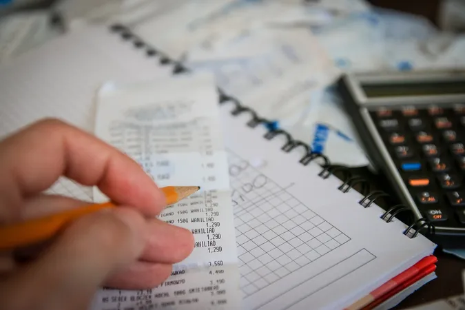 An image of a hand holding a pencil, going through a receipt with a notepad and calculator