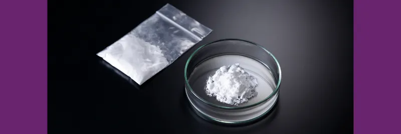 White powder in a dish and in a small plastic bag sit on a black surface
