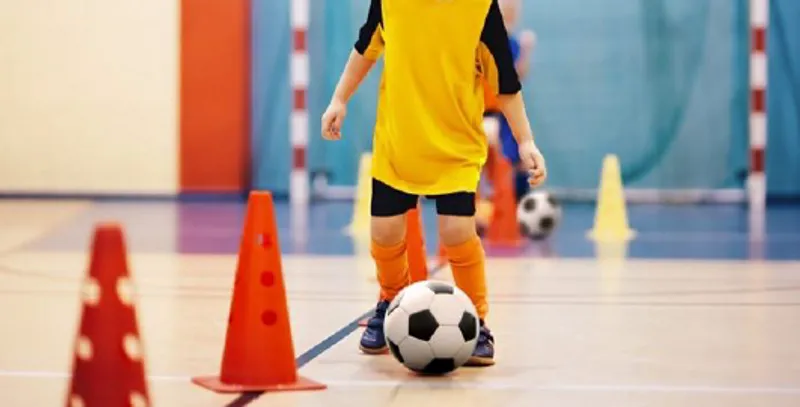 A child kicking a football at a holiday club in a school gymnasium