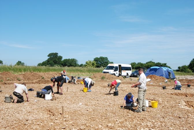 Group of students looking for artefacts, with a minibus in background