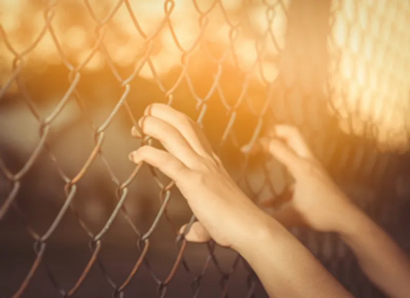 Hands holding onto a chain link fence