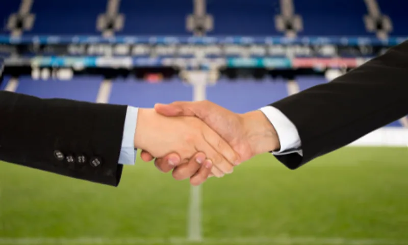Shaking hands in front of a football pitch
