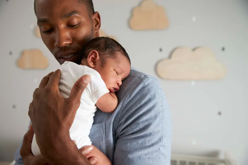 Man cradling his baby in a child's bedroom.