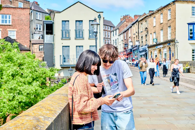 Two students looking at a phone in Durham City on a bridge