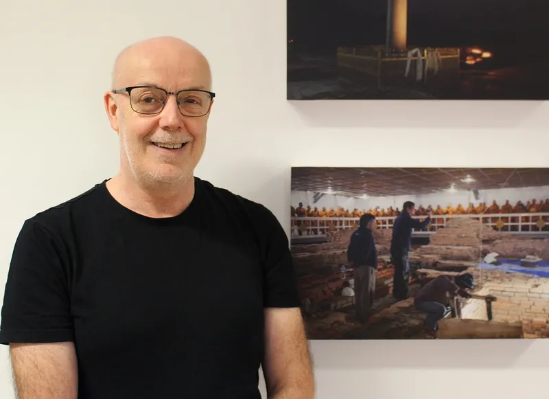 Craig Barclay standing in front of images of archaeological excavation