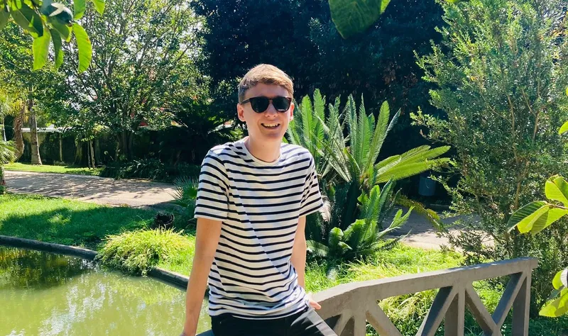 Photo of man in striped t shirt and sunglasses, surrounded by plants and trees