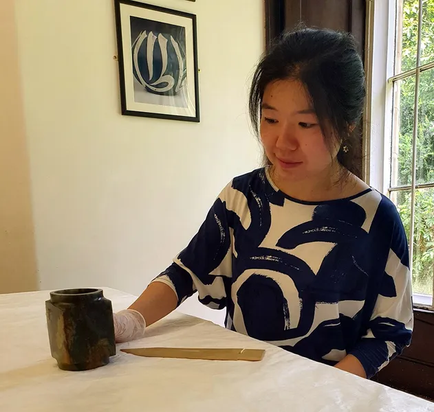 Qin Cao sitting at a table looking at Chinese jade objects