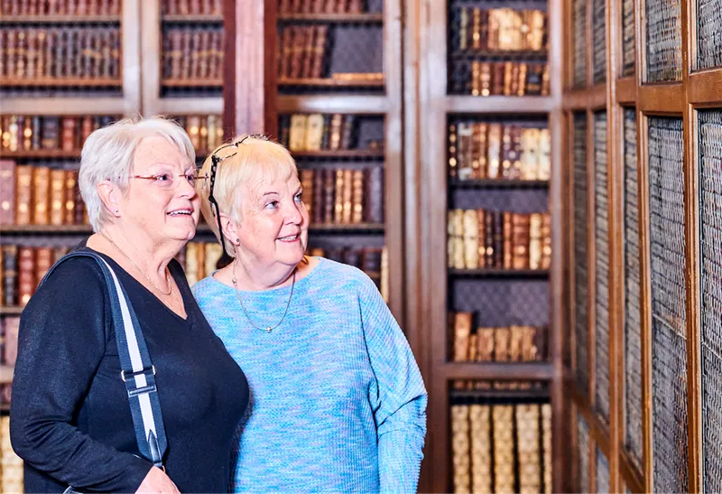 Two ladies stand smiling looking at the bound rare books of Bishop Cosin's Library