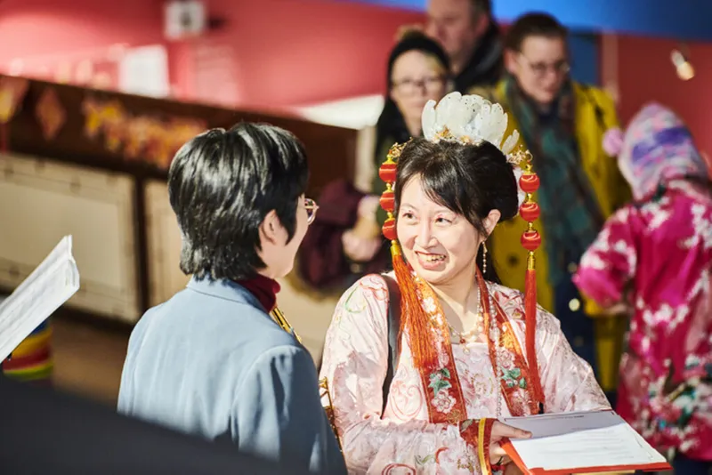 Person in traditional costume from China talks to a student musician (they have their back to the camera)