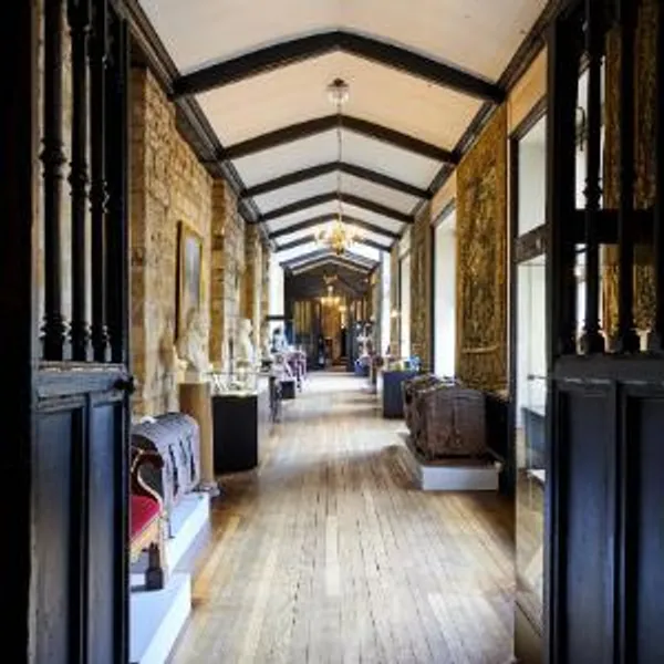 View along the length of the Tunstall Gallery inside Durham Castle. Along the length of the Gallery are tapestries, paintings, busts of famous figures, old wood and metal chests and museum cases.