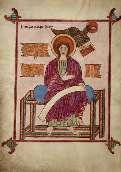 View of the portrait page of St John from the Lindisfarne Gospels, showing him sat facing front holding a scroll in one hand, with his other hand on his chest. His symbol, an eagle, is shown behind his head