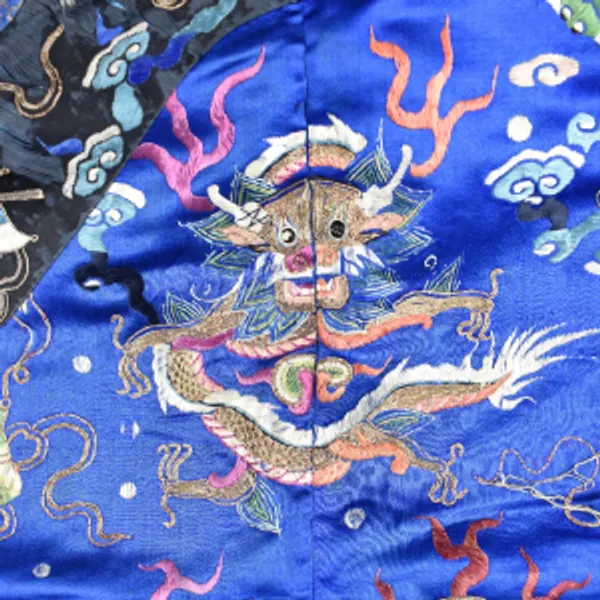 Zoomed in view of a detail on an imperial Chinese robe showing a Chinese dragon on a blue background surrounded by various symbols.