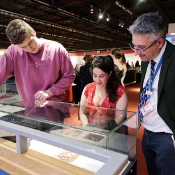 Three people are looking at a piece of art within a glass museum case.