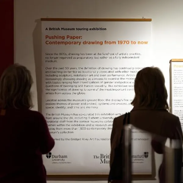 Two exhibition visitors reading the Pushing Paper exhibition information