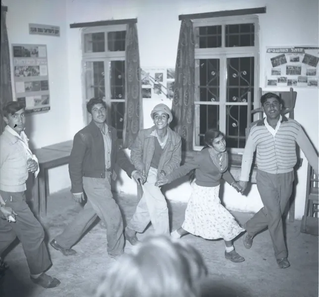 A group of people holding hands and dancing around a living room.