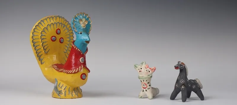 Group of three toys, one is a large yellow and blue rooster, and the smaller two are a black horse and a white fantasy creature with two heads.
