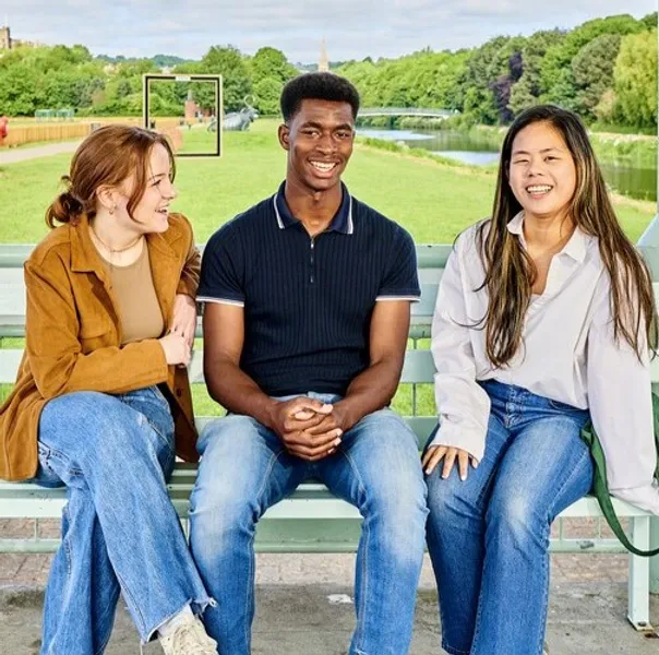 A diverse group of students smiling and posing on a bench in front of a playing field