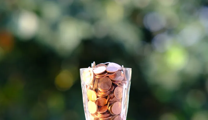 A glass filled with coins with blurry trees behind
