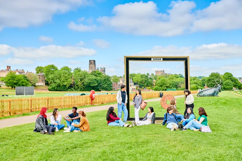 Groups of students sitting and standing on grass with Durham Cathedral in the background