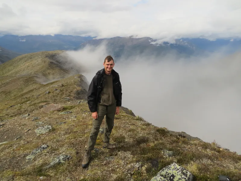 Dr Smith stands on a high mountainous ridge, surrounded by mist