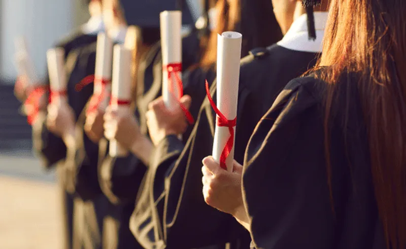 Graduates in a row from behind holding a scroll with red ribbon