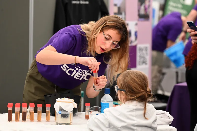 A Celebrate Science volunteer helps a child do and experiment with testtubes.