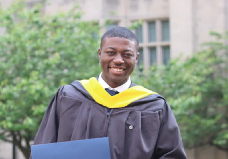 Alumnus Enoch Omale smiling at camera in congregation robes