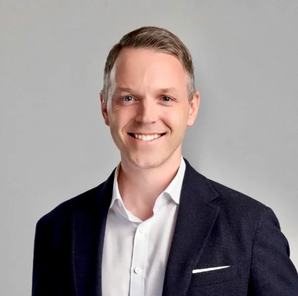 A man wearing a suit jacket and white shirt smiling at the camera