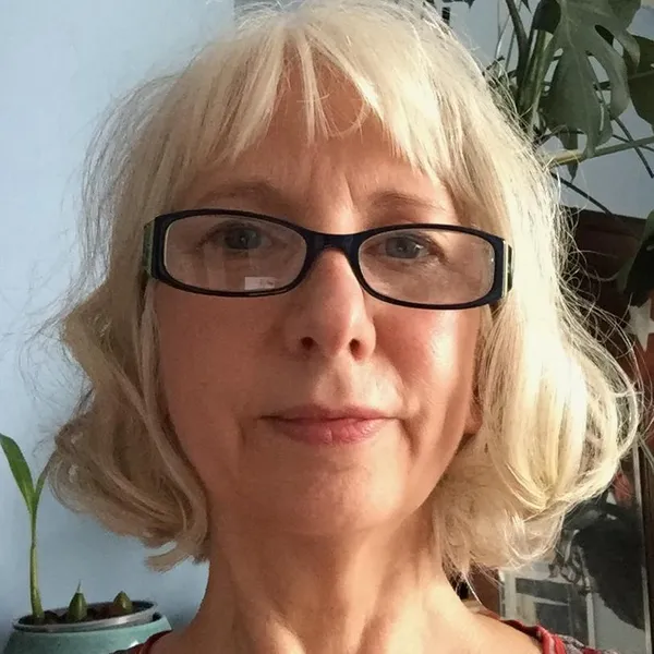 A women with light hair and black framed glasses looking straight at the camera