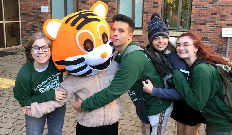 Brooks House, 3 storey student accommodation, modern building with 3 student Fresher’s Reps hugging Cuth's Tiger mascot.