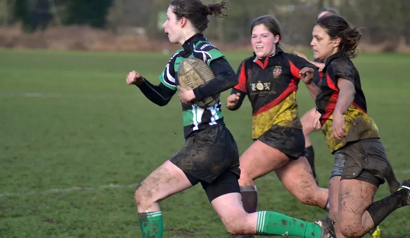 Cuth’s female rugby player in green kit running with a rugby ball and being chased by 2 opponents.