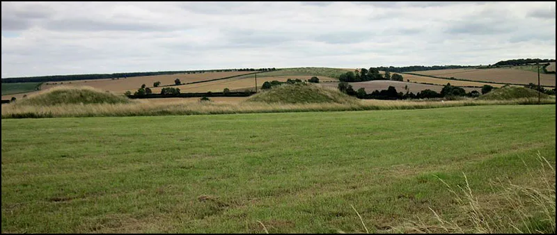 Two burial mounds in a field with hills in the background