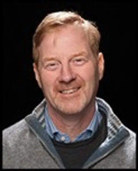 Staff profile photo of Robin Skeates smiling in front of a plain black background.