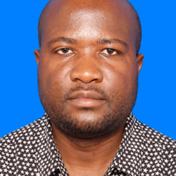 Front facing portrait photo of Dr Elgidius Ichumbaki, against a bright blue background.