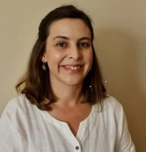 Portrait photo of Dr Abigail Moffett smiling in front of a light beige wall.