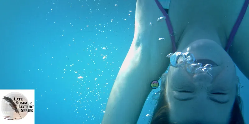 A woman swims upside down underwater with bubbles emerging from her nose