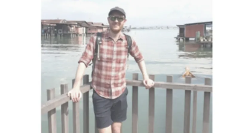 Image of a male graduate wearing a checked shirt, hat and sunglasses.